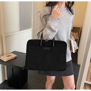 Detail of black nylon laptop briefcase with leather logo held by a model in office setting