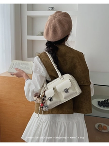 Close-up of minimalist white shoulder bag with twin front pockets and cute bear charm
