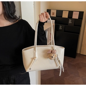 Dettaglio della borsa tote crema testurizzata con doppi manici e ciondolo a forma di orsetto