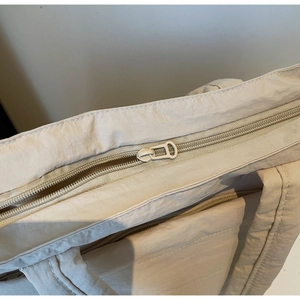 Detail view of the metal zipper closure and reinforced stitching on beige shoulder bag