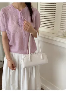 Close-up of a white leather bowling bag carried by a model in a minimal interior