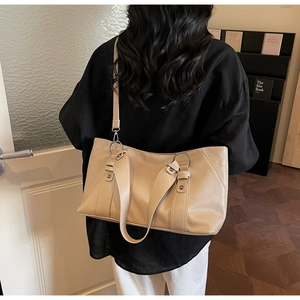 Detail of light beige tote bag featuring silver metal rings and detachable strap on a model