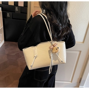 Dettaglio borsa tote bianco sporco con texture a mano e ciondolo a forma di orsetto