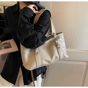 Detail view of a beige tote bag featuring vertical strap accents and metallic ring hardware