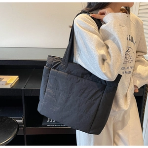 Close-up of black quilted puffer tote bag showing padded texture and side pocket detail