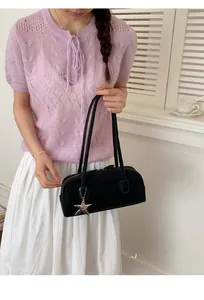 Detail view of a black leather baguette bag with a silver star charm on a casual shoulder strap