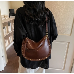 Detail of vintage brown crescent bag with gold rivets shown on model in a cozy room