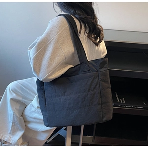 Detail of a large black quilted tote bag showing nylon texture and horizontal stitching
