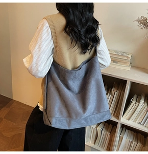 Rear view of a model carrying the large grey suede tote bag in a minimalist library setting