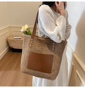 Detail of hand-woven straw tote bag with brown leather pocket and long shoulder straps