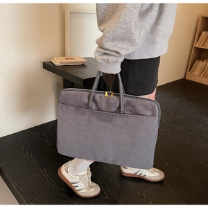 Close-up of a grey suede laptop bag with dual zippers and a dark grey handle in a lifestyle setting