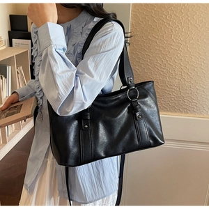 Detail of black faux leather tote bag with silver metal rings and rivets on shoulder strap