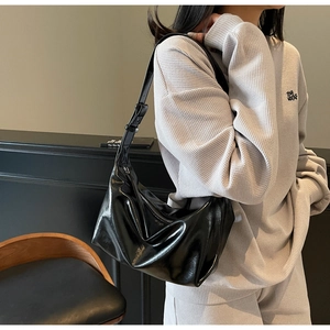 Detailed close-up of glossy black leather hobo bag with adjustable silver buckle strap