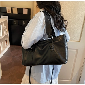 Detail of black faux leather tote bag with wide strap and metallic silver ring accents