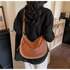 Detail of a brown leather crescent tote bag with golden rivets and adjustable shoulder strap