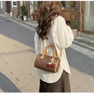 Detail of vintage brown cylinder bag with yellow handles and cherry pendant on a street