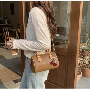 Brown cylinder Boston bag with cherry charm shown in a cozy cafe lifestyle setting