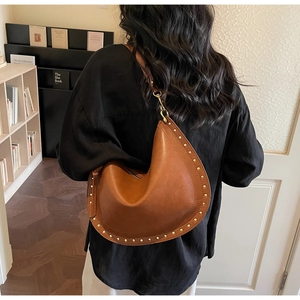 Detail of vintage brown crescent bag featuring gold stud rivets and smooth leather finish