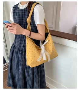 Detail view of yellow polka dot canvas tote bag with white lace bow and hobo style strap