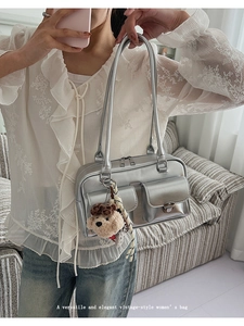 Silver metallic handbag with dual flap pockets and a plush brown bear pendant