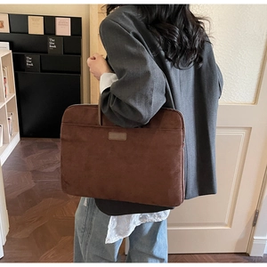 Rear view of a dark brown suede laptop bag held by a person in a home office setting