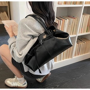 Détail d'un grand sac cabas noir brillant avec de fines bandoulières dans une bibliothèque