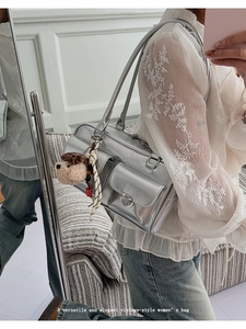 Detail view of a silver metallic vintage shoulder bag with front pockets and teddy charm