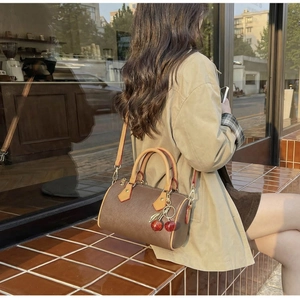 Classic patterned Boston barrel bag with red cherry charm accessory on a cafe background