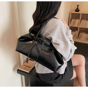Sac fourre-tout noir brillant chic porté avec un sweat à capuche gris en intérieur