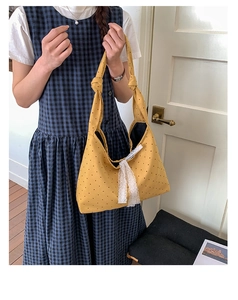Close-up of yellow polka dot canvas tote bag featuring lace bow and knotted shoulder strap