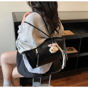 Dettaglio della borsa tote nera lucida con texture stropicciata, nappe e ciondolo morbido