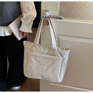 Detail of beige nylon tote bag with functional pockets and textured fabric on white door