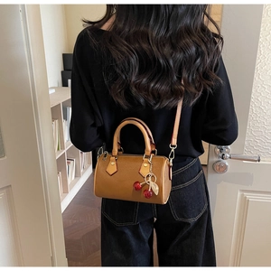 Detail view of brown leather crescent bag with cherry pendant and adjustable strap