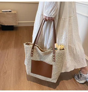 Detail of hand-woven straw tote bag with brown leather shoulder straps and front pocket