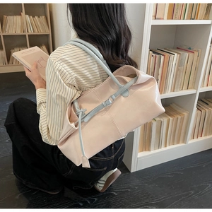 Détail d'un grand sac fourre-tout rose clair avec anses bleues dans une bibliothèque