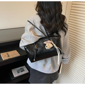 Dettaglio della borsa tote nera con trama in pelle increspata e ciondolo a forma di cucciolo