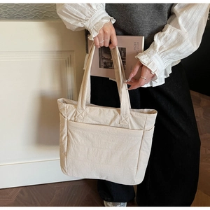 Detail shot of the beige tote bag showing crinkled texture and front compartment pocket