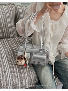 Detail view of a vintage silver shoulder bag with double pockets and a plush bear charm