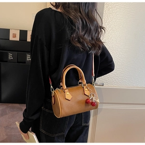 Close-up of a mini brown Boston bag with a cute cherry charm and detachable shoulder strap