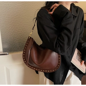 Brown leather crescent bag with gold rivet details worn over the shoulder in a casual style