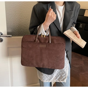 Close-up of brown suede laptop bag with leather handles and metallic zipper detail