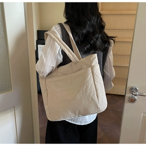 Detail view of beige tote bag showing texture and front pocket during daily commute