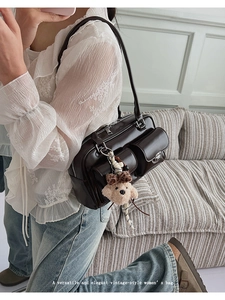 Detail view of dark brown patent leather shoulder bag with a cute plush bear pendant