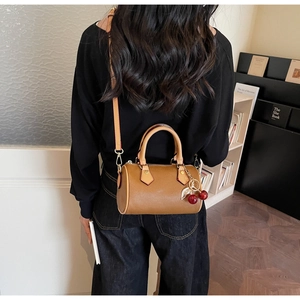 Detail of tan leather cylinder bag with red cherry charm worn by a model in interior