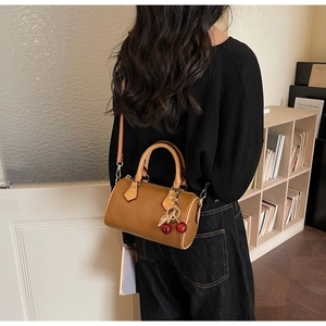 Detailed shot of brown boston style bag with golden hardware and cherry pendant detail