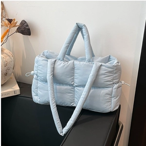 Light blue quilted down tote bag with dual straps and side drawstring on furniture