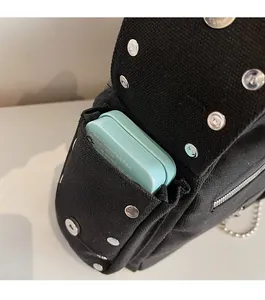 Detail of black canvas bag side pocket with silver snap buttons and metal chain decor