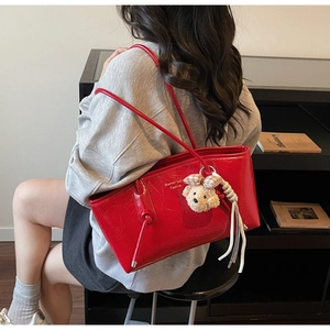 Dettaglio borsa tote in pelle verniciata rossa con ciondolo a orsetto e trama lucida