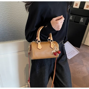 Close-up of brown cylinder Boston bag with gold hardware and cherry charms