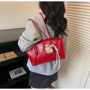 Dettaglio borsa shopper rossa con trama lucida e ciondolo a forma di orsetto sulla tracolla